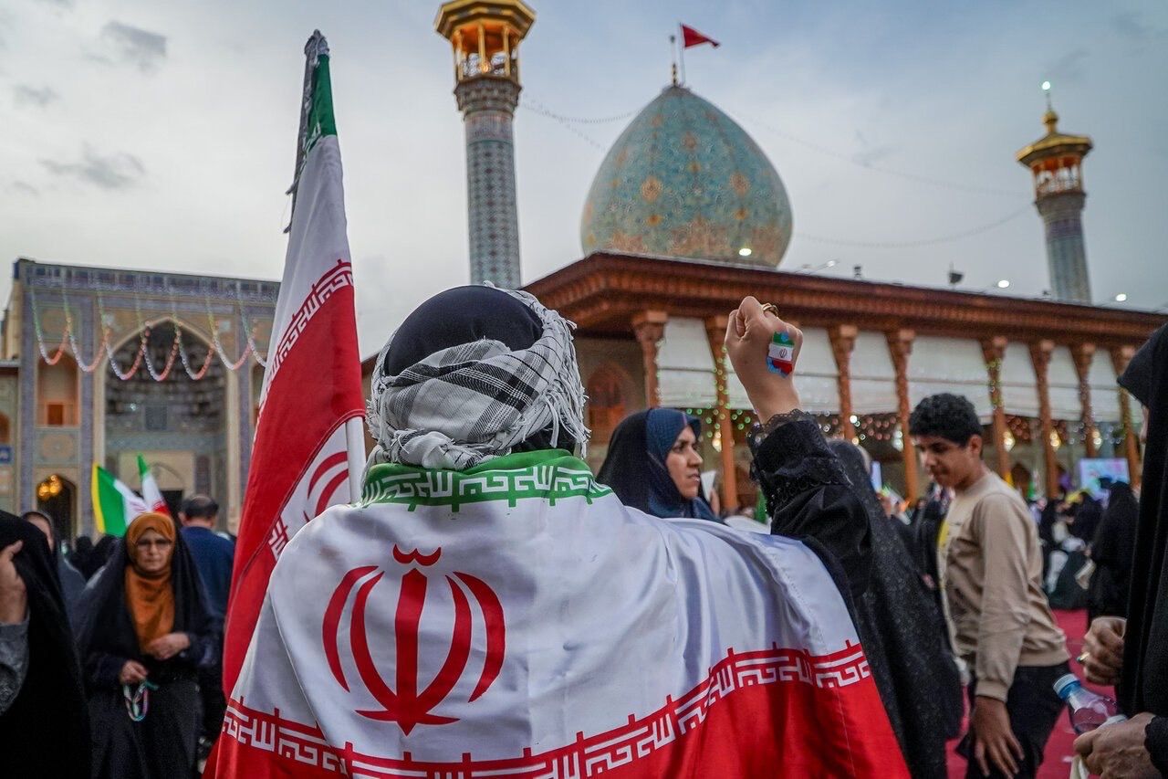 A Tehran loyalist wraps herself in Iran's flag, at a state-sponsored rally, April 2026