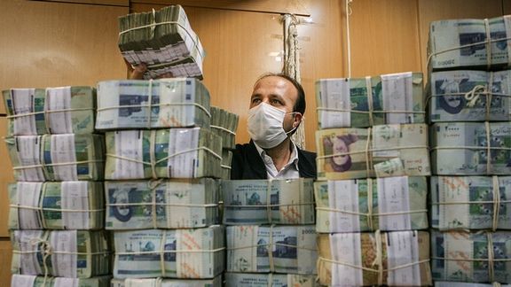 An Iranian man sitting behind a pile of national currency banknotes