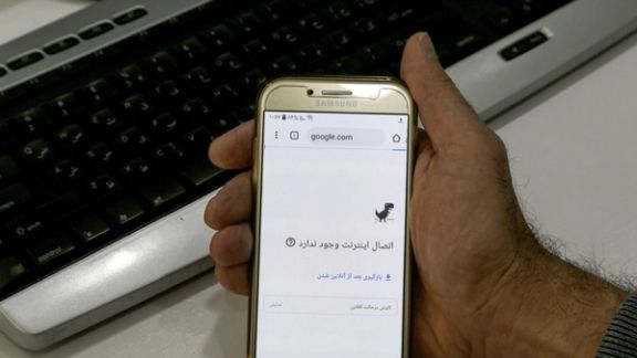 An Iranian user holds up a mobile phone displaying a "No Internet Connection" error message.