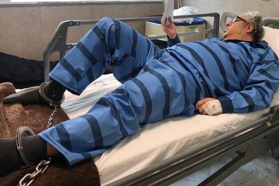 بکتاش آبتین روی تخت بیمارستان با لباس زندان و پاهای بسته به زنجیر