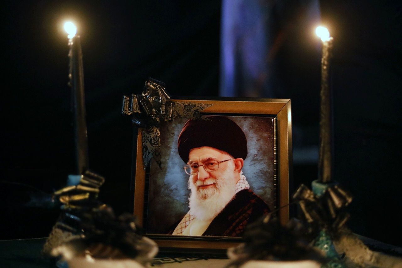 A framed portrait of Iran's slain Supreme Leader Ali Khamenei is displayed beside lit candles during a mourning ceremony.