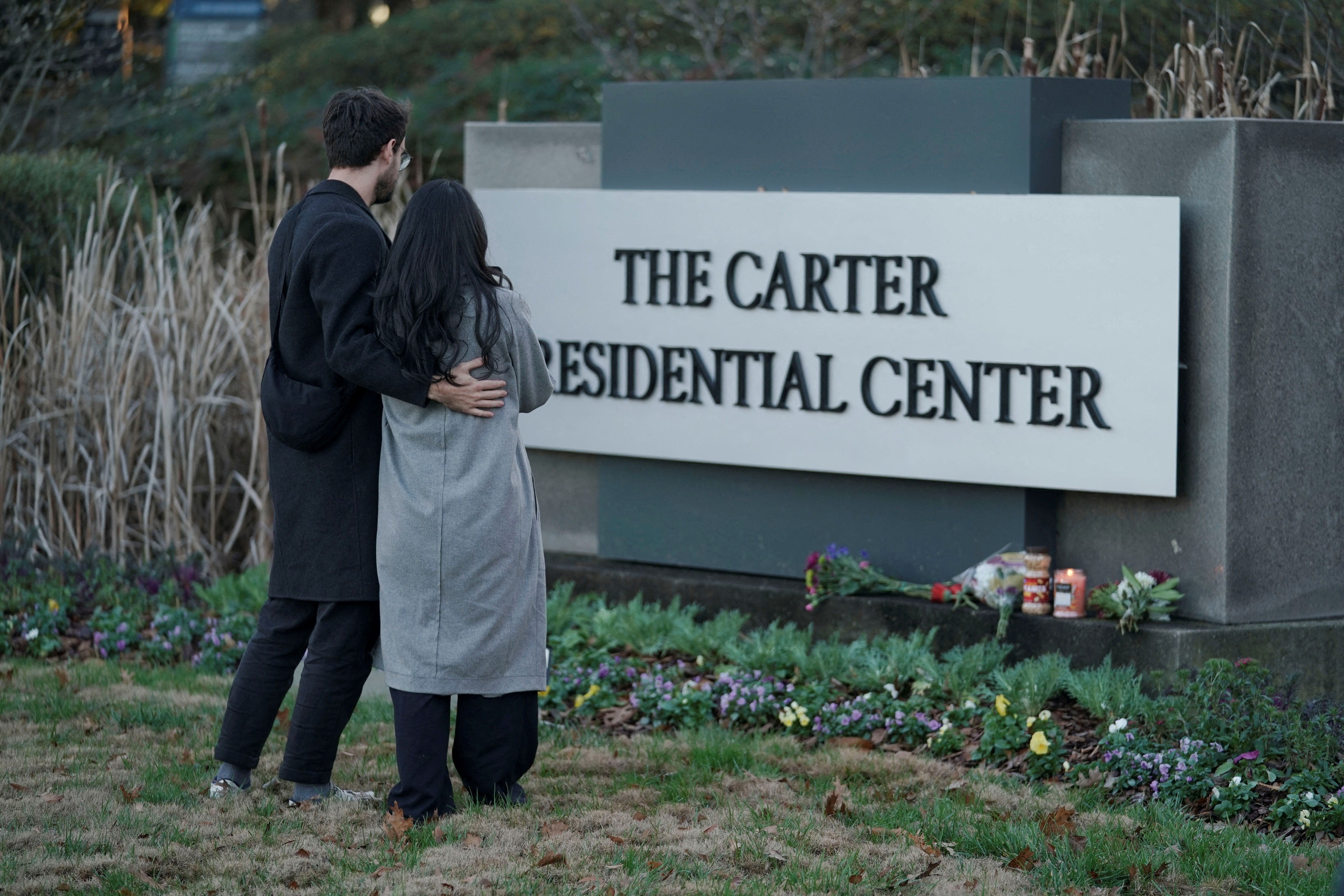 A couple stands in front of The Carter Presidential Center's sign, after the death of former US President Jimmy Carter at the age of 100, in Atlanta, Georgia, December 29, 2024. 