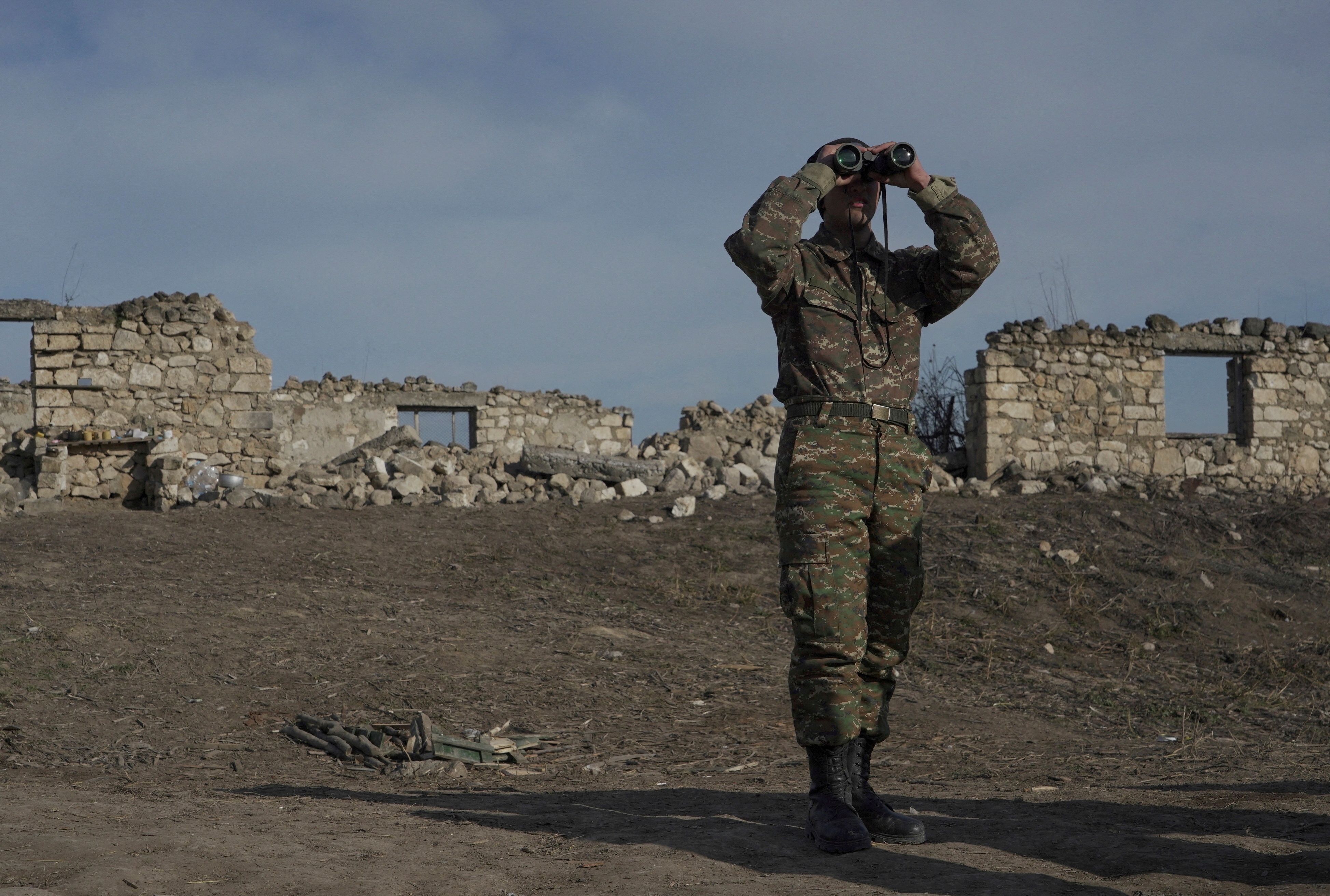 An ethnic Armenian soldier looks through binoculars as he stands at fighting positions near the village of Taghavard in the region of Nagorno-Karabakh, January 11, 2021. 