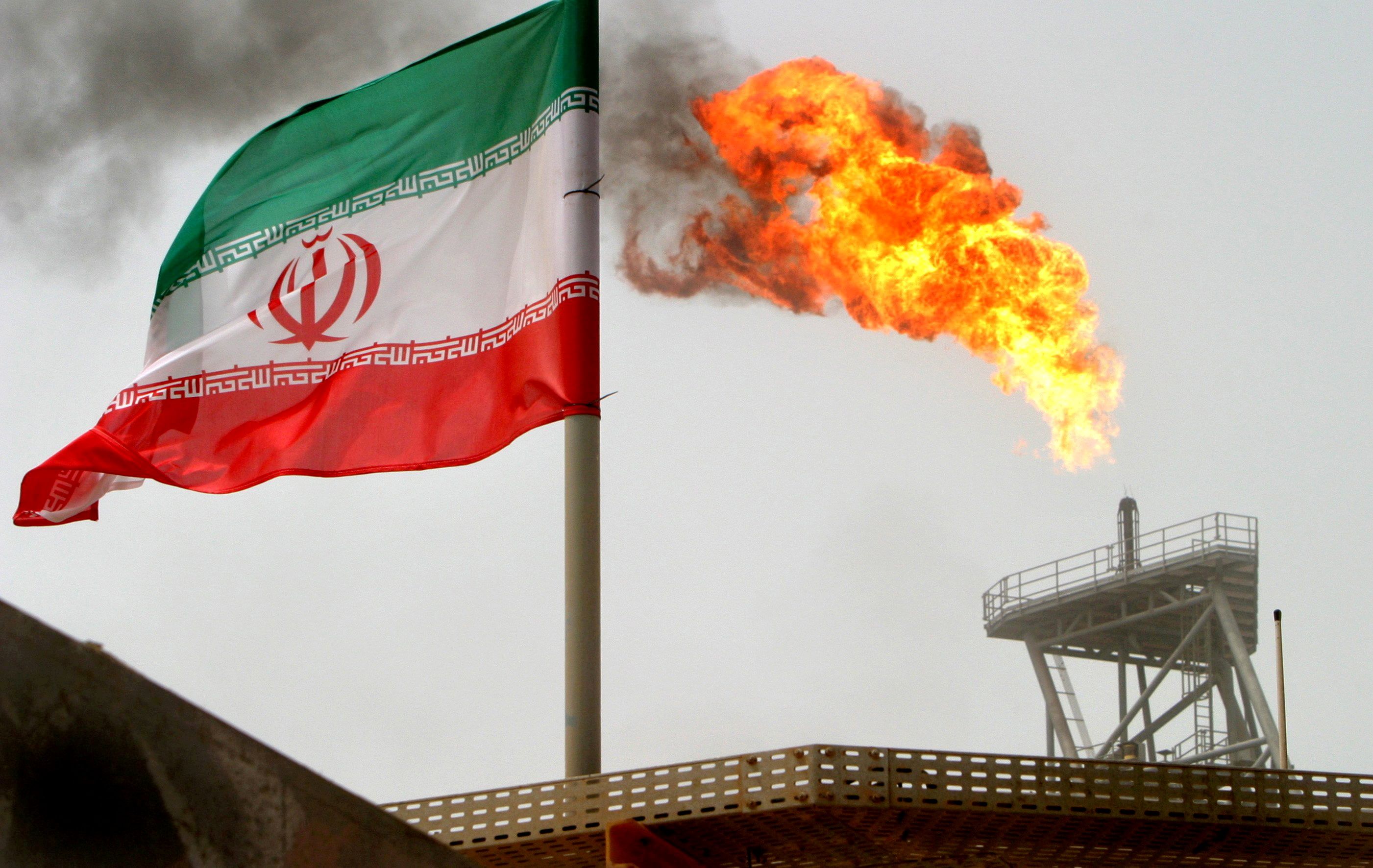A gas flare on an oil production platform is seen alongside an Iranian flag in the Persian Gulf July 25, 2005. 