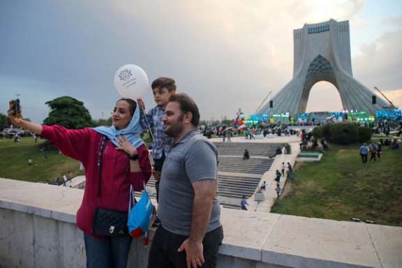 A family takes a selfie near Tehran’s Azadi Tower during a state-sponsored gathering in the capital, June 2026