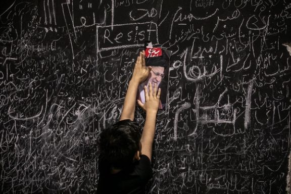 A child places a picture of Ali Khamenei among handwritten messages left by mourners on a memorial wall set up during funeral ceremonies in Tehran, July 5, 2026