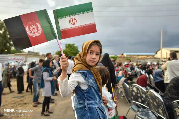 An Afghan girl holding the flags of the Islamic Republic of Iran and Afghanistan