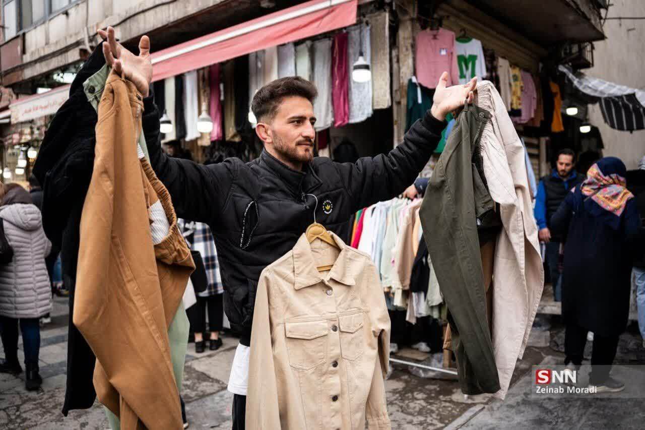 A retailer in Tehran's Grand Bazaar holds up clothes to attract attention, March 2025
