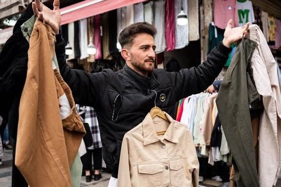 A retailer in Tehran's Grand Bazaar holds up clothes to attract attention, March 2025