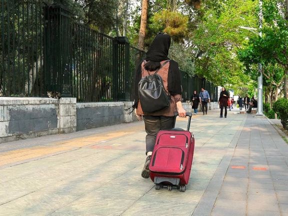 A woman with a suitcase walks outside the University of Tehran, Iran.