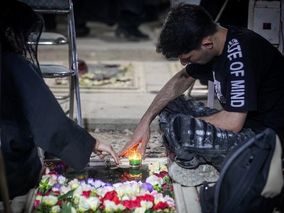 A man and woman sit by the grave of their loved one, Tehran, Iran, July 3, 2025