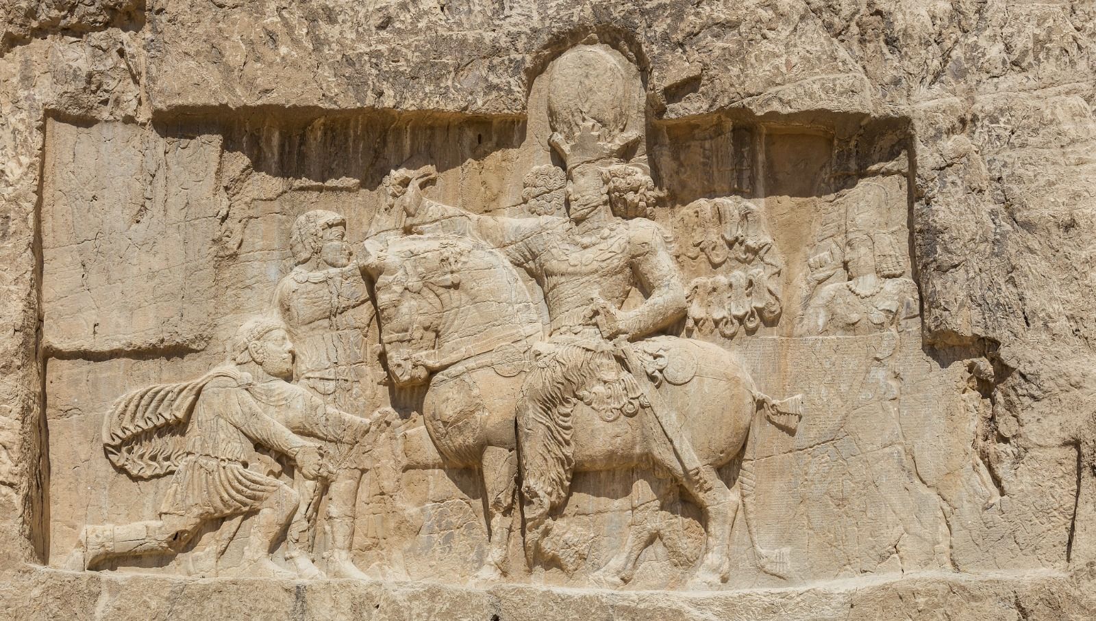 An ancient rock face relief at Naqsh-e Rostam shows Emperor Shapur on horseback compelling the captive Roman Emperor Valerian to kneel.